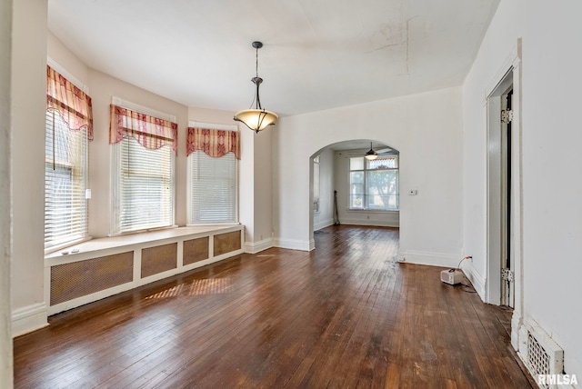 unfurnished dining area with arched walkways, visible vents, baseboards, and hardwood / wood-style flooring