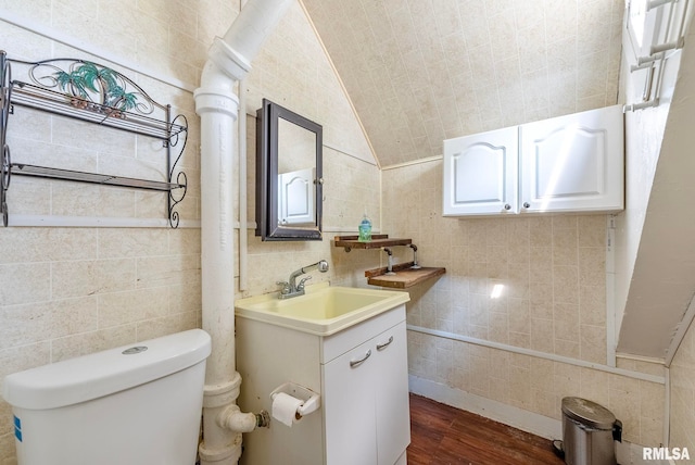 half bathroom with toilet, wood finished floors, tile walls, vanity, and vaulted ceiling