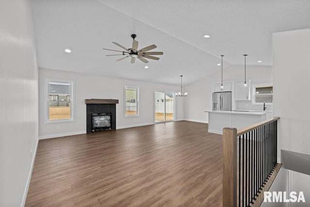 unfurnished living room with lofted ceiling, dark hardwood / wood-style floors, and ceiling fan with notable chandelier