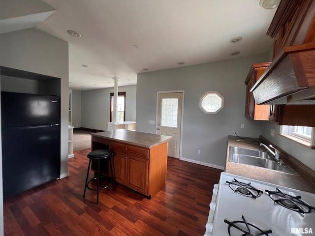 kitchen featuring white range with gas cooktop, a kitchen bar, black refrigerator, sink, and dark wood-type flooring