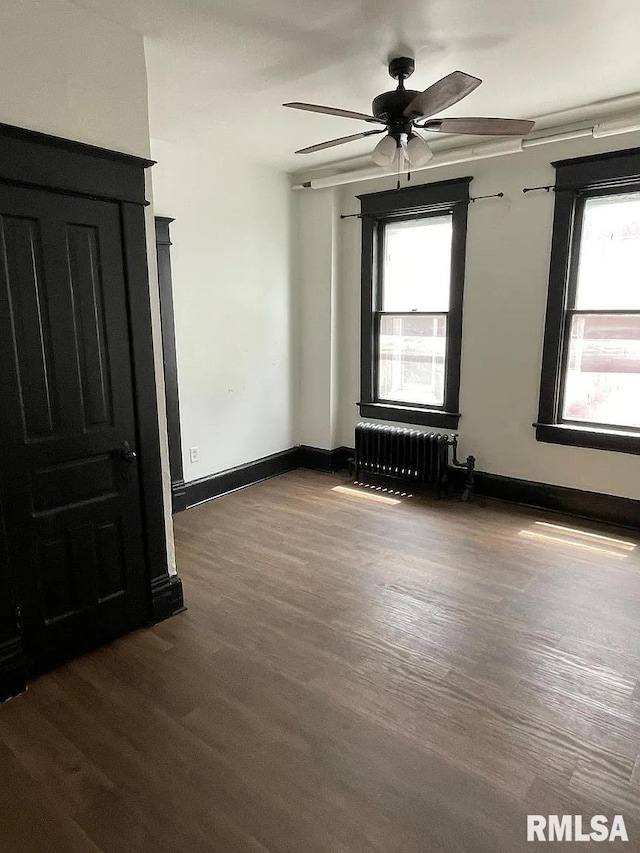 empty room featuring ceiling fan, dark hardwood / wood-style floors, and radiator heating unit