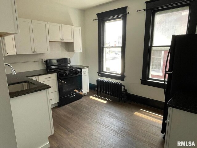 kitchen featuring dark wood-type flooring, black appliances, a wealth of natural light, and radiator heating unit