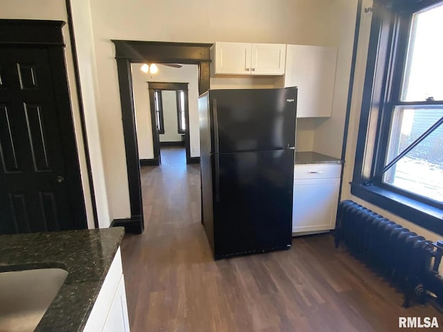 kitchen with dark wood-type flooring, white cabinetry, a wealth of natural light, and black fridge