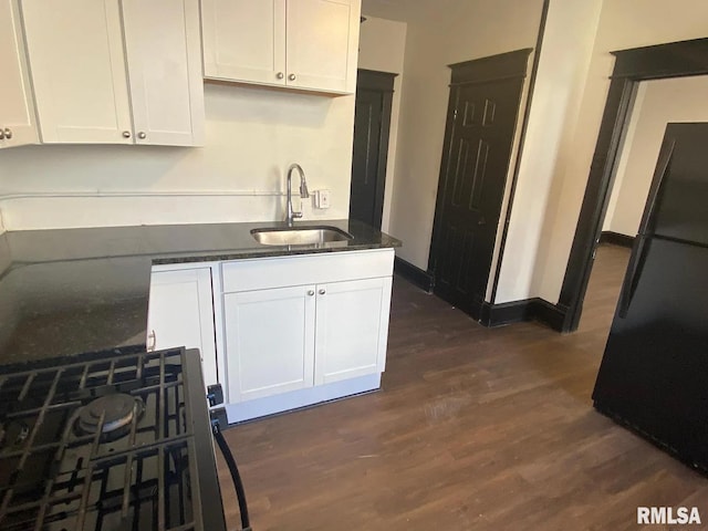 kitchen with dark wood-type flooring, white cabinetry, black refrigerator, and sink