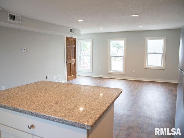 kitchen featuring a textured ceiling, hardwood / wood-style floors, white cabinetry, and light stone countertops