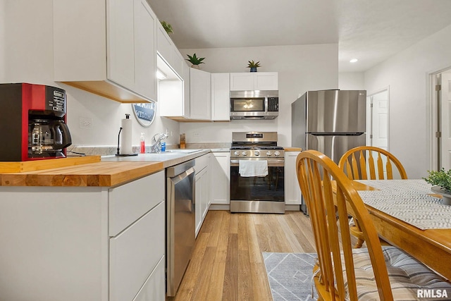 kitchen with stainless steel appliances, butcher block counters, a sink, light wood-style floors, and white cabinets