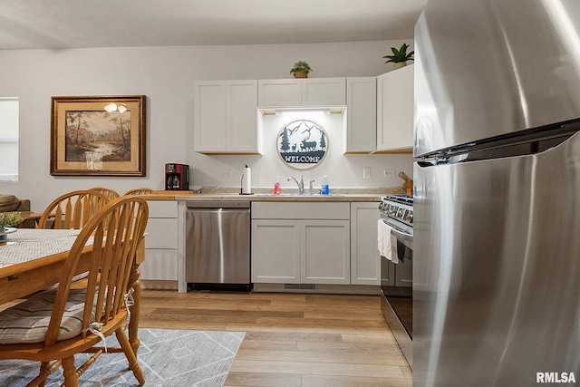 kitchen with light wood-type flooring, sink, stainless steel appliances, and white cabinets