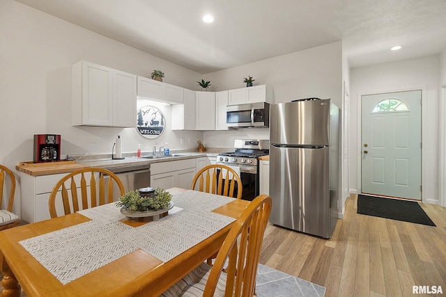 kitchen featuring light wood finished floors, stainless steel appliances, light countertops, white cabinetry, and a sink