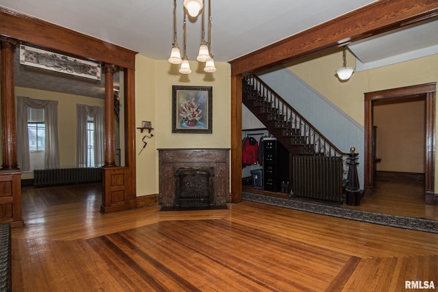 unfurnished living room with beam ceiling, decorative columns, radiator heating unit, a high end fireplace, and hardwood / wood-style flooring