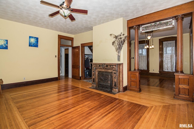 unfurnished living room with a textured ceiling, ceiling fan with notable chandelier, wood finished floors, baseboards, and decorative columns