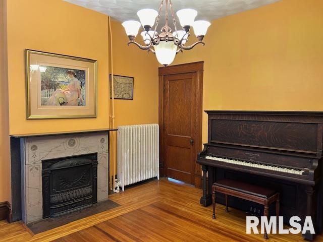 sitting room featuring a fireplace with flush hearth, a chandelier, radiator heating unit, and wood finished floors