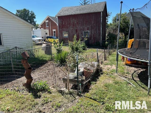 view of yard with a trampoline, fence, and a garden