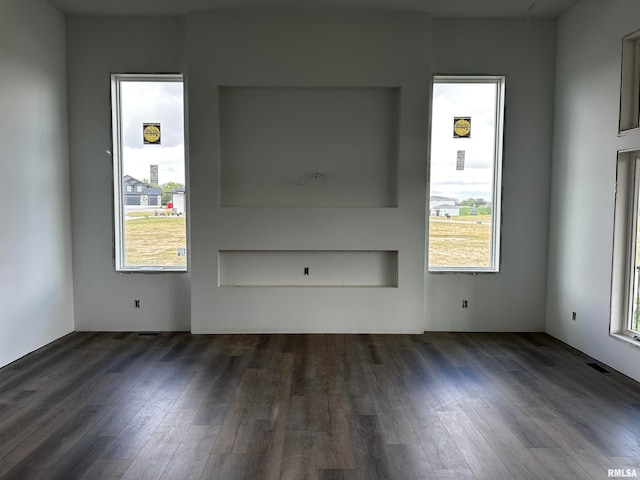 unfurnished living room featuring plenty of natural light and dark hardwood / wood-style floors