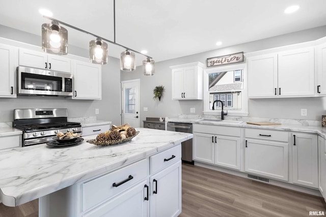 kitchen featuring decorative light fixtures, appliances with stainless steel finishes, a center island, sink, and white cabinets