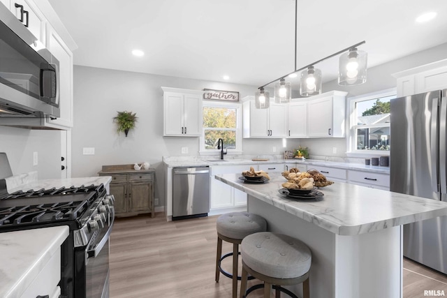 kitchen with white cabinets, hanging light fixtures, light wood-type flooring, stainless steel appliances, and a kitchen island