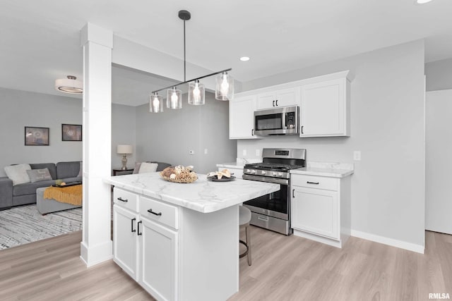 kitchen with appliances with stainless steel finishes, decorative light fixtures, white cabinets, and light hardwood / wood-style floors