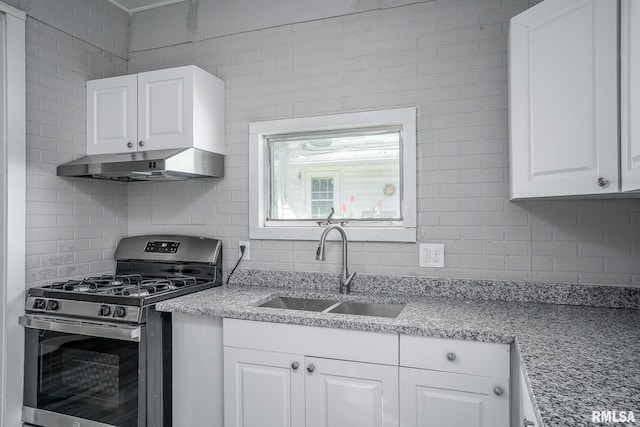 kitchen with gas stove, light stone counters, white cabinetry, brick wall, and sink