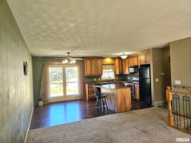 kitchen featuring a breakfast bar area, dark hardwood / wood-style floors, black appliances, a center island, and ceiling fan