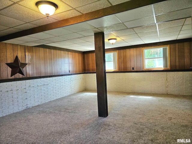 basement featuring wood walls, brick wall, carpet flooring, and a paneled ceiling