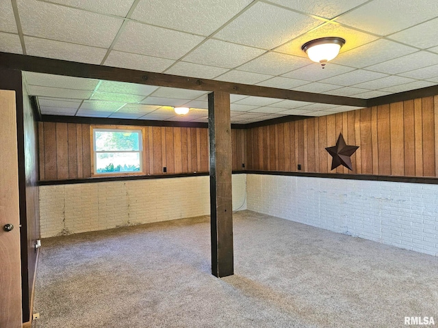 basement featuring a paneled ceiling, carpet flooring, wooden walls, and brick wall