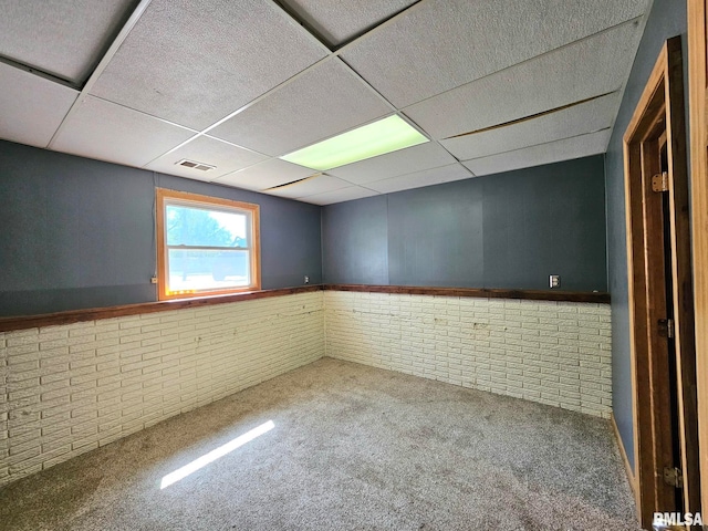 spare room featuring carpet floors, a drop ceiling, and brick wall