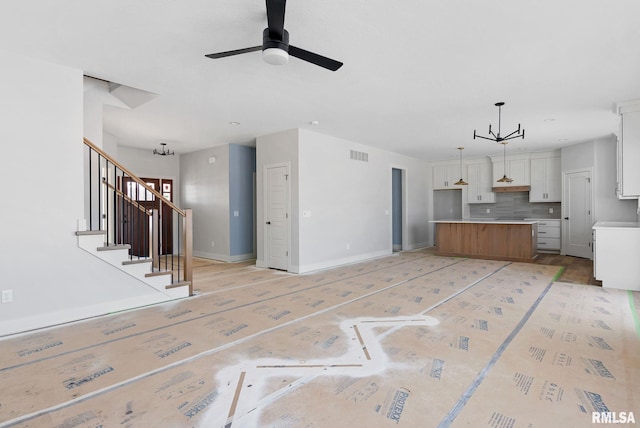 unfurnished living room featuring ceiling fan with notable chandelier and light wood-type flooring