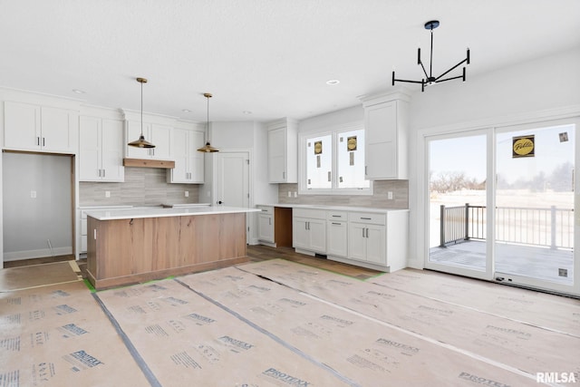 kitchen featuring white cabinets, decorative light fixtures, decorative backsplash, a kitchen island, and an inviting chandelier