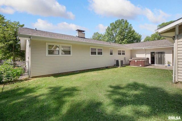 rear view of property featuring a yard, central AC, and a hot tub