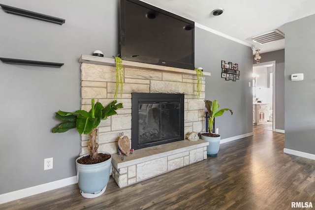living room featuring dark wood-type flooring, crown molding, and a stone fireplace