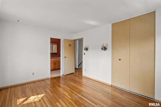 unfurnished bedroom with ensuite bath, a closet, and light wood-type flooring