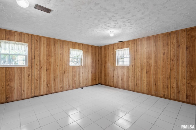 tiled empty room with a textured ceiling, plenty of natural light, and wood walls