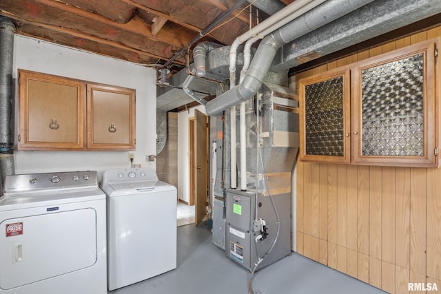 clothes washing area with cabinets, wooden walls, heating unit, and washer and clothes dryer