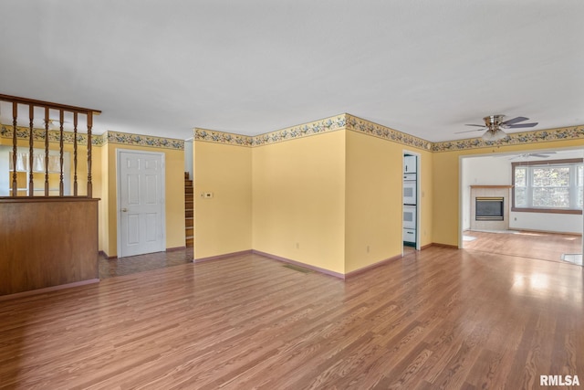 unfurnished room with ceiling fan, a tiled fireplace, and hardwood / wood-style floors