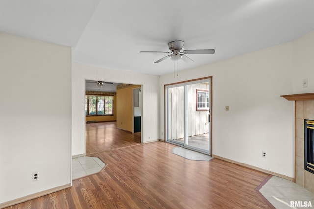 interior space with ceiling fan, a tiled fireplace, and wood-type flooring