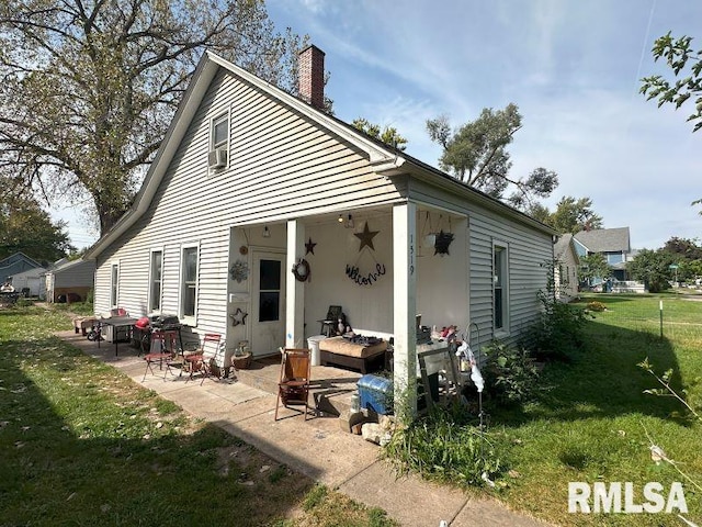 rear view of property featuring a patio area, a lawn, and a chimney