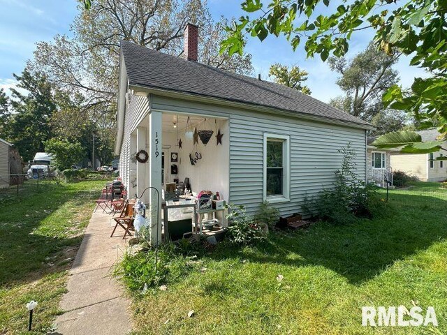 back of house with fence, a lawn, a shingled roof, and a chimney
