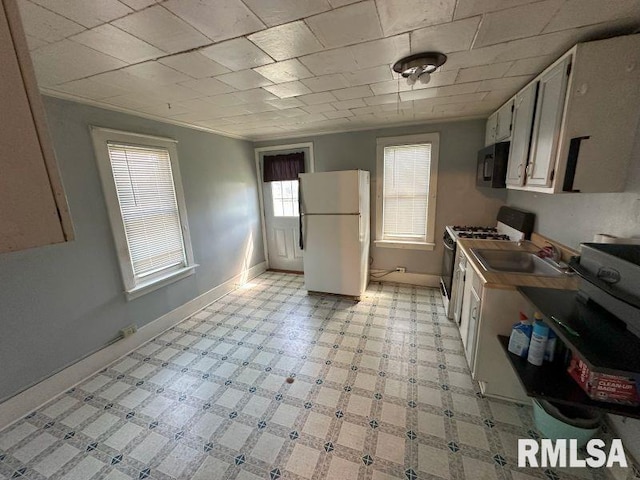 kitchen with a sink, black microwave, gas range oven, baseboards, and freestanding refrigerator