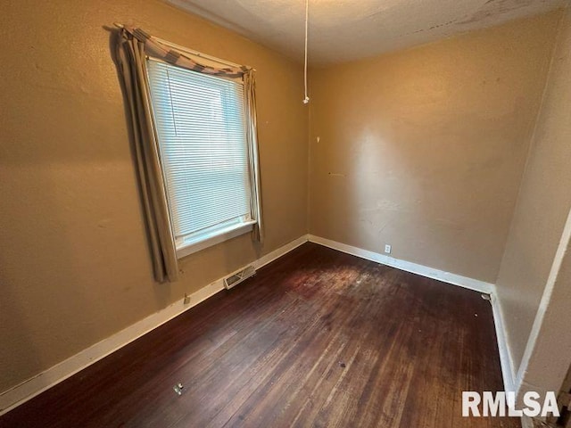unfurnished room with baseboards, dark wood-style flooring, and visible vents