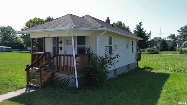 bungalow with a shingled roof, covered porch, a chimney, and a front lawn