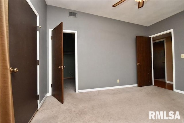 unfurnished bedroom with a walk in closet, ceiling fan, light colored carpet, and a closet