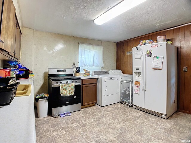 kitchen with washing machine and dryer, white refrigerator with ice dispenser, wood walls, a textured ceiling, and stainless steel range