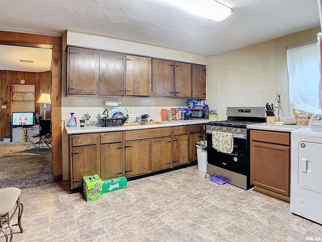 kitchen featuring wooden walls, sink, washer / dryer, and stainless steel range