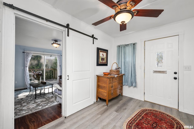 entrance foyer with ceiling fan, light hardwood / wood-style flooring, crown molding, and a barn door