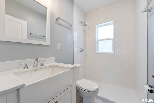 bathroom featuring a tile shower, vanity, and toilet