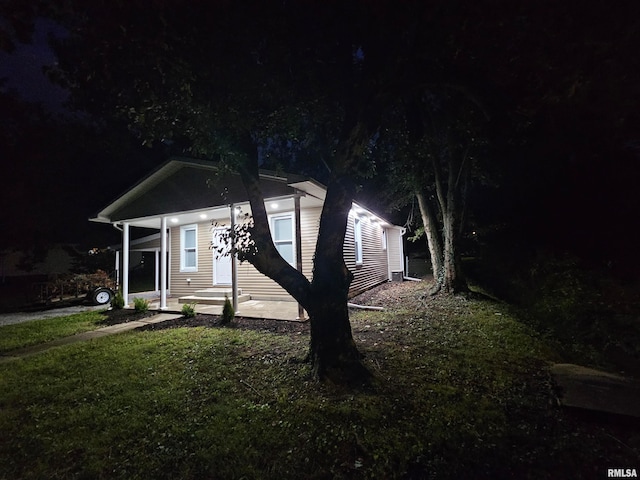 property exterior at night with a lawn and covered porch