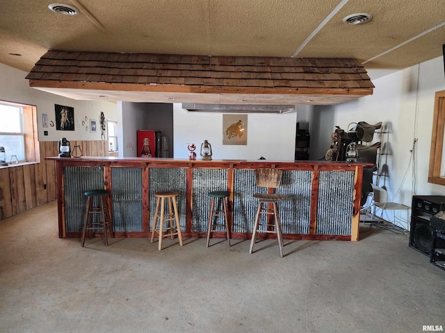 bar with wood walls, concrete flooring, and a textured ceiling