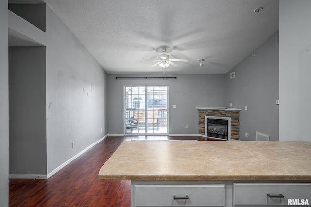 kitchen with a textured ceiling, ceiling fan, dark wood-type flooring, and a stone fireplace