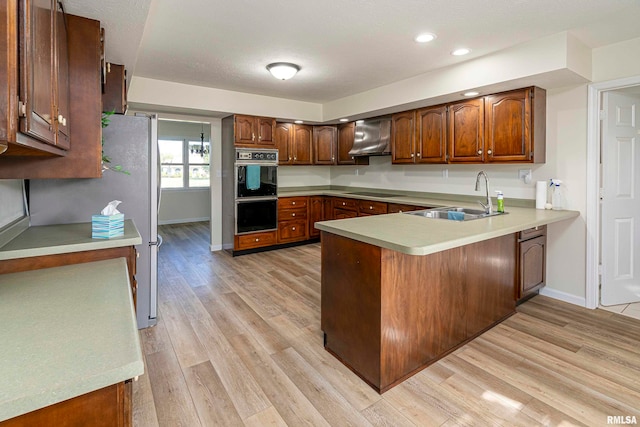 kitchen with light wood-type flooring, sink, kitchen peninsula, and black appliances