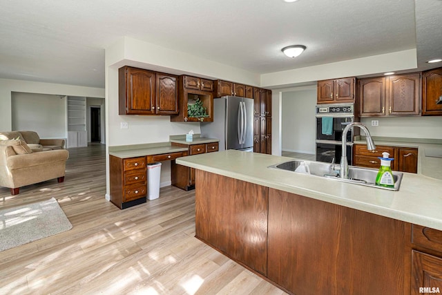 kitchen with stainless steel refrigerator, light wood-type flooring, a textured ceiling, double oven, and sink