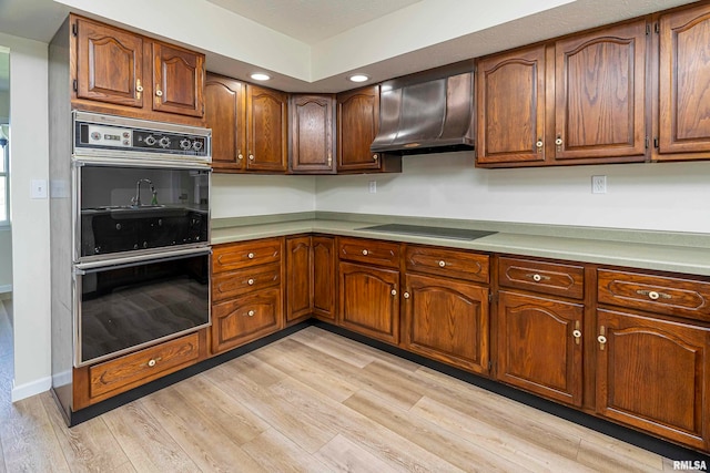 kitchen featuring light hardwood / wood-style floors, wall chimney range hood, and black appliances